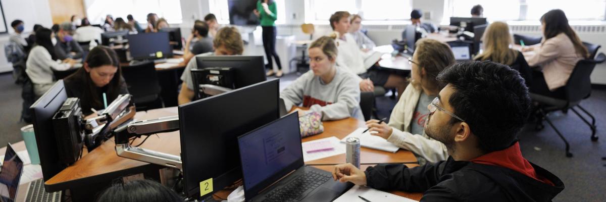 Several students are seen inside a computer lab sitting in front of computers studying
