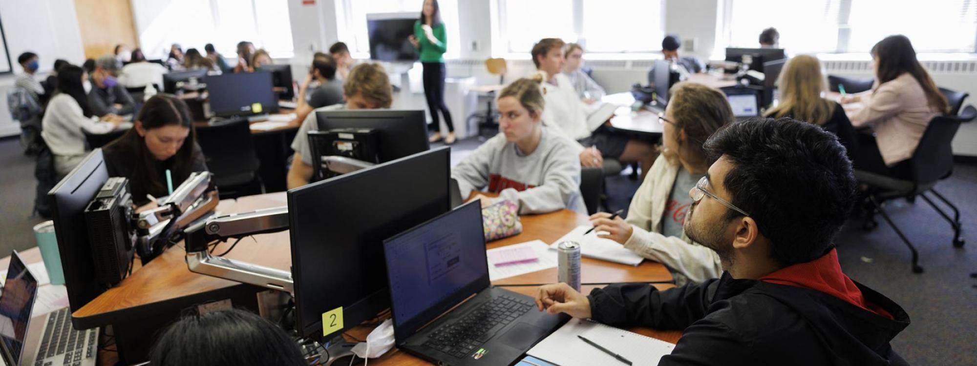 Several students are seen inside a computer lab sitting in front of computers studying